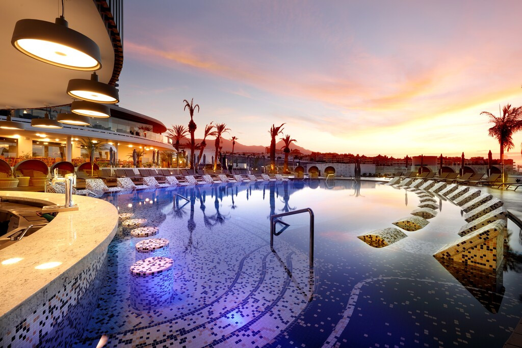 Zwembad bij zonsondergang in een hotel op Tenerife, met moderne verlichting en ligstoelen.