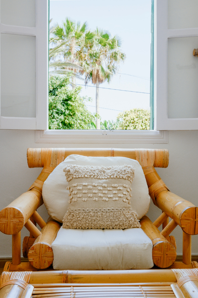 Rotanen fauteuil met kussen in de woonkamer voor een open raam met uitzicht op een palmboom op Tenerife.