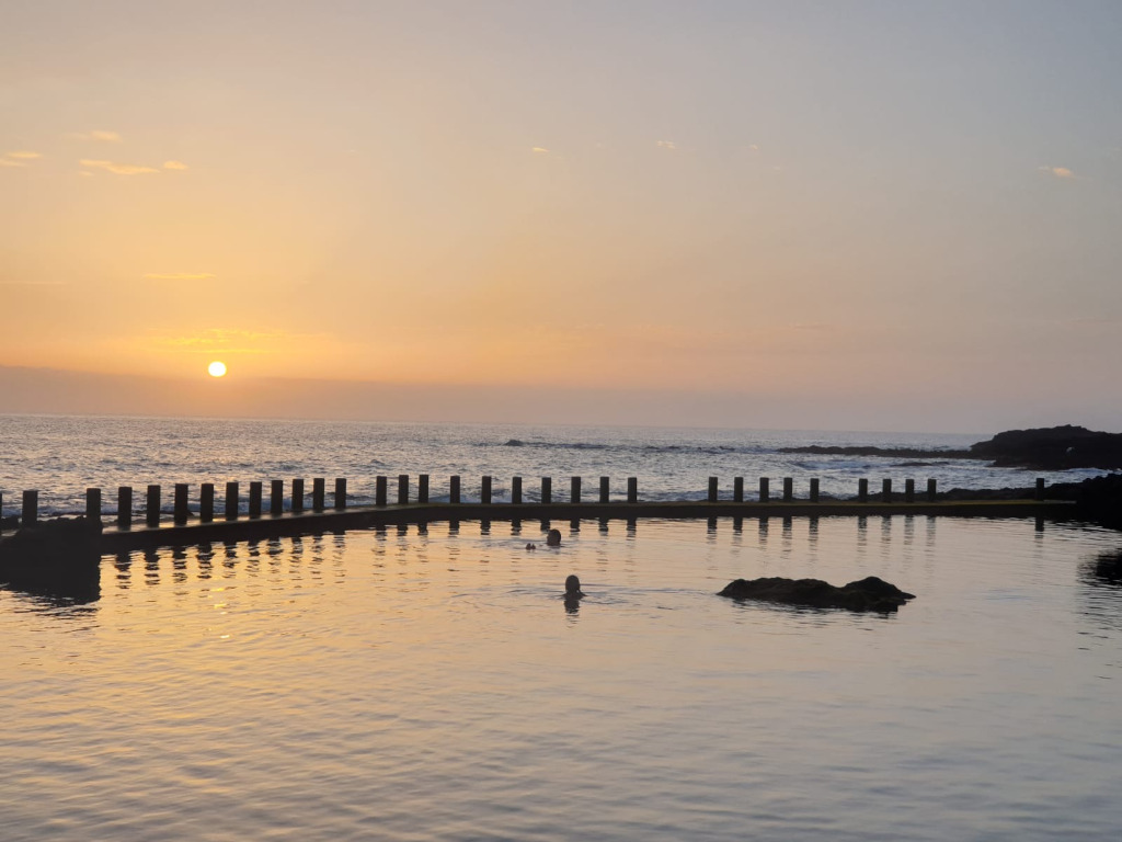 Zonsondergang in het natuurlijke zwembad van Tenerife met mensen die zwemmen.
