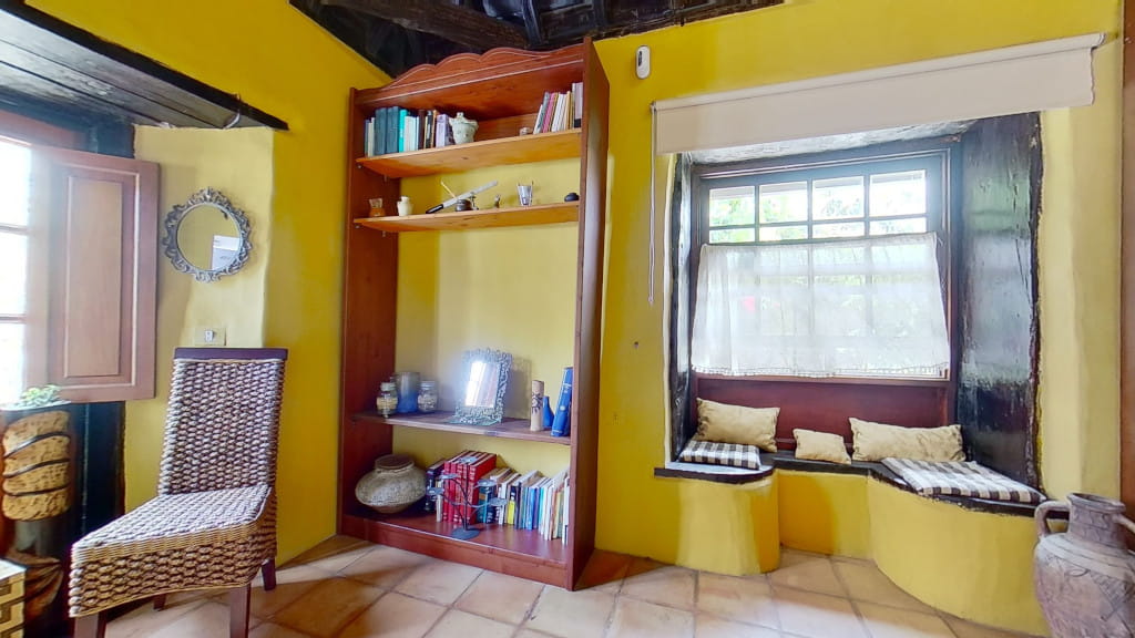 Gele kamer op Tenerife met plank, gevlochten stoel en raam met geruite kussens.