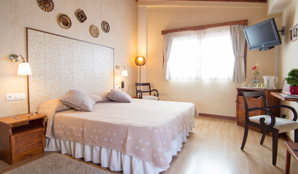 Een lichte tweepersoonskamer met groot bed, tv en houten meubels op Tenerife.