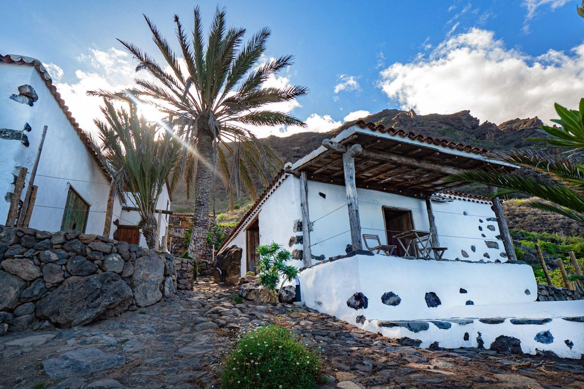 Landhuis met palmbomen in Masca, Tenerife, onder een blauwe lucht en bergen op de achtergrond.