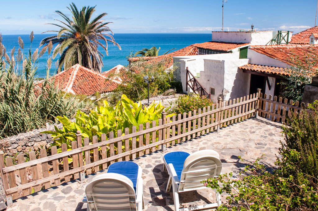 Terras met stoelen en zeezicht op Tenerife, omringd door planten en palmbomen.