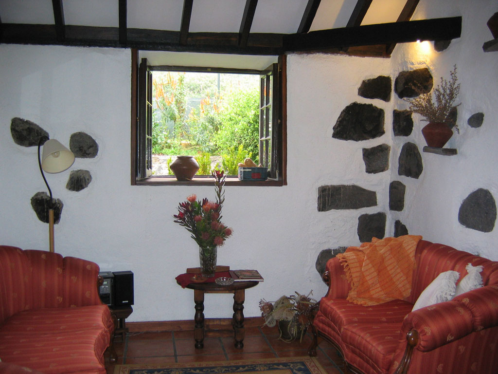Rustieke woonkamer op Tenerife met rode bank, raam en buitenplanten.