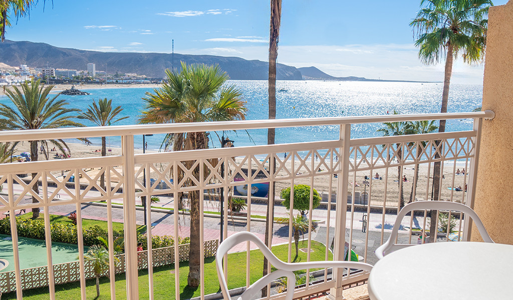Uitzicht vanaf een balkon richting het strand van Los Cristianos op Tenerife, met zee- en palmbomen.