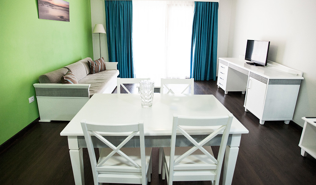 Woonkamer met witte tafel, bank, tv en gordijnen in een appartement op Tenerife.
