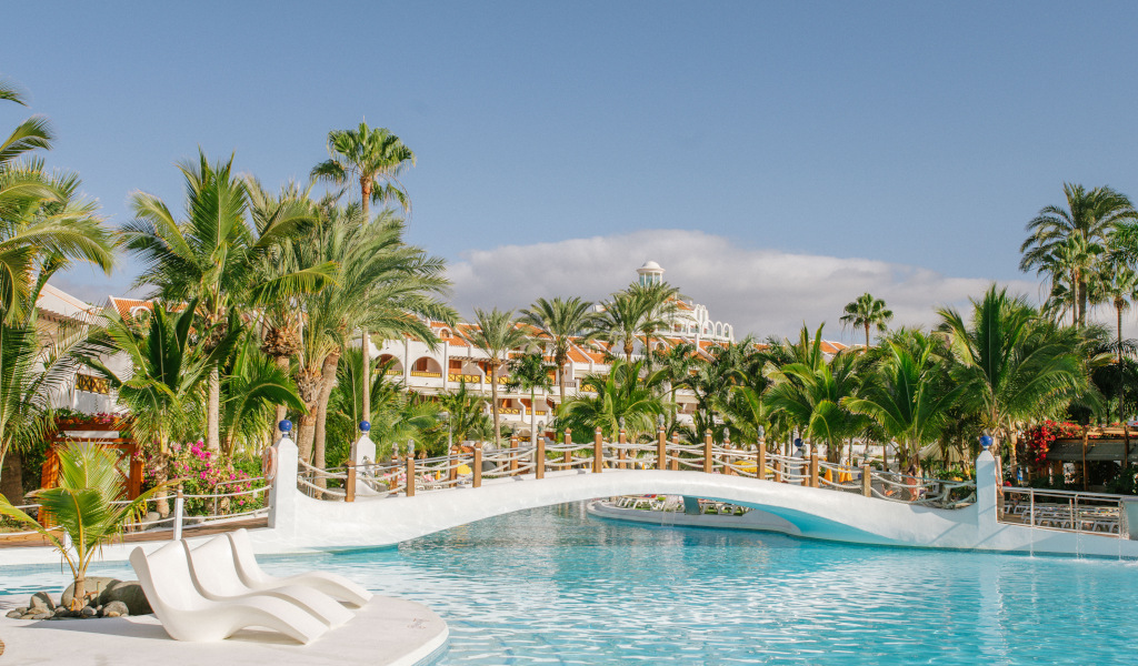 Zwembad en brug omringd door palmbomen in een hotelcomplex op Tenerife.