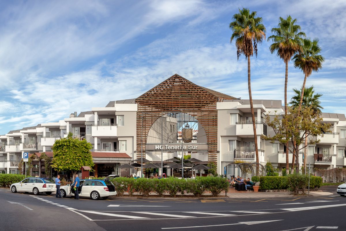 Hoofdingang van HC Tenerife Zuid met taxi's en palmbomen aan de straat.