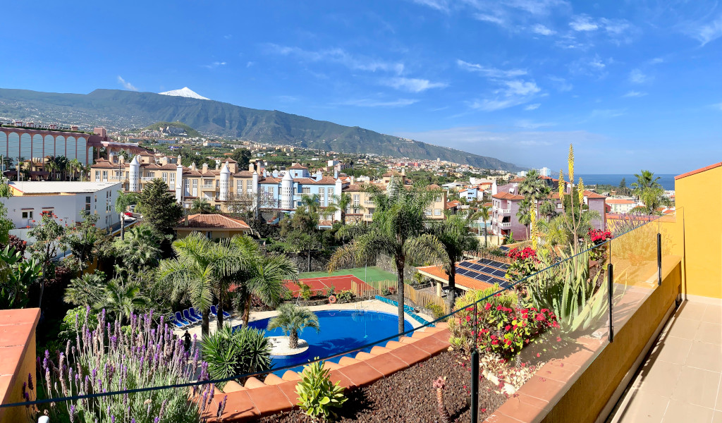 Uitzicht op Puerto de la Cruz op Tenerife met een zwembad, palmbomen en Teide op de achtergrond.