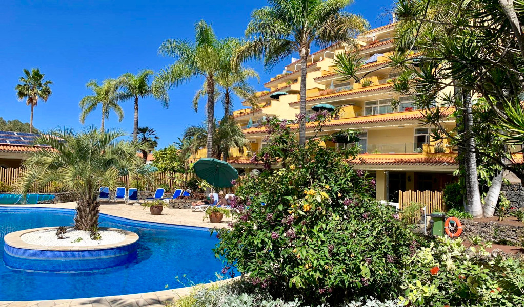 Zwembad omringd door palmbomen en een appartementencomplex op Tenerife.