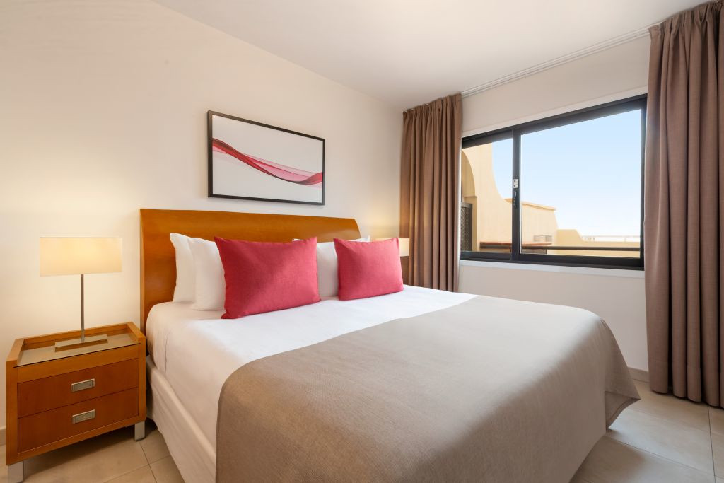 Hotelkamer op Tenerife met een tweepersoonsbed, rode kussens en een groot raam.
