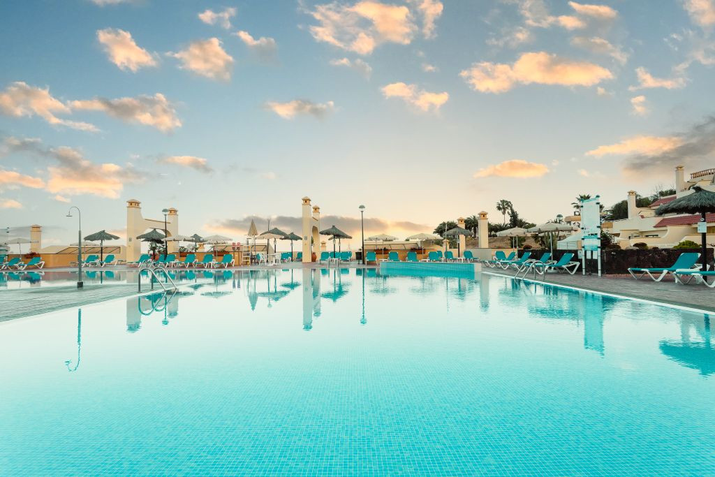 Buitenzwembad bij zonsondergang op Tenerife, omringd door ligstoelen en parasols.