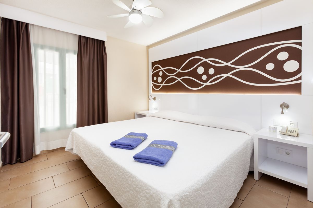 Tweepersoonsbed met blauwe handdoeken en muurdecoratie in een hotel op Tenerife.