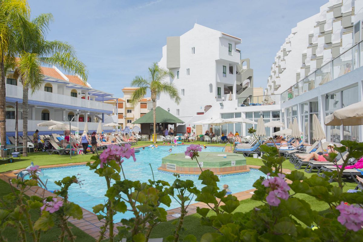 Hotelzwembad op Tenerife met gasten die rusten en bouwen op de achtergrond.