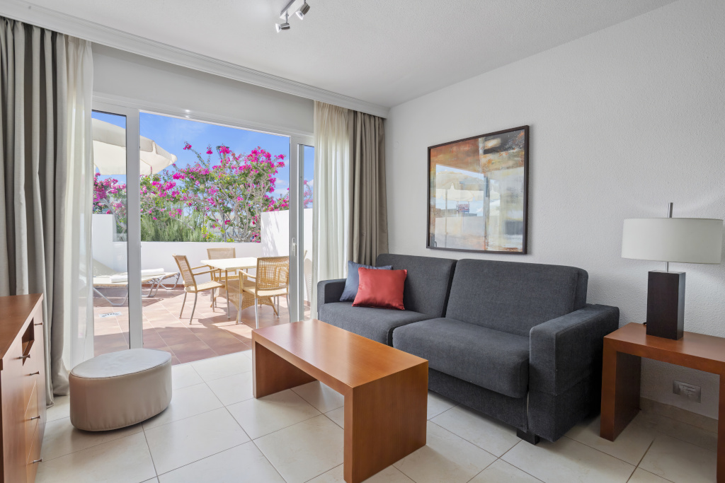 Woonkamer met grijze bank en uitzicht op het terras met bloemen op Tenerife.