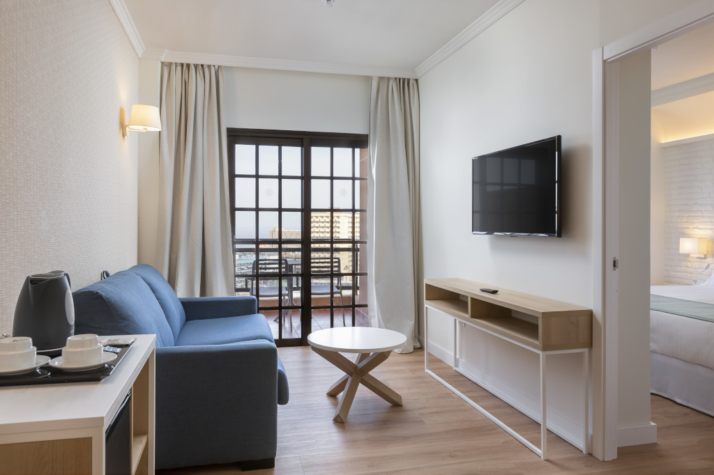 Hotelwoonkamer op Tenerife met blauwe bank en aan de muur gemonteerde tv.