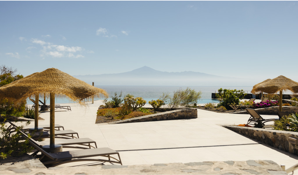 Terras met parasols en ligstoelen op Tenerife, uitzicht op zee en bergen op de achtergrond.