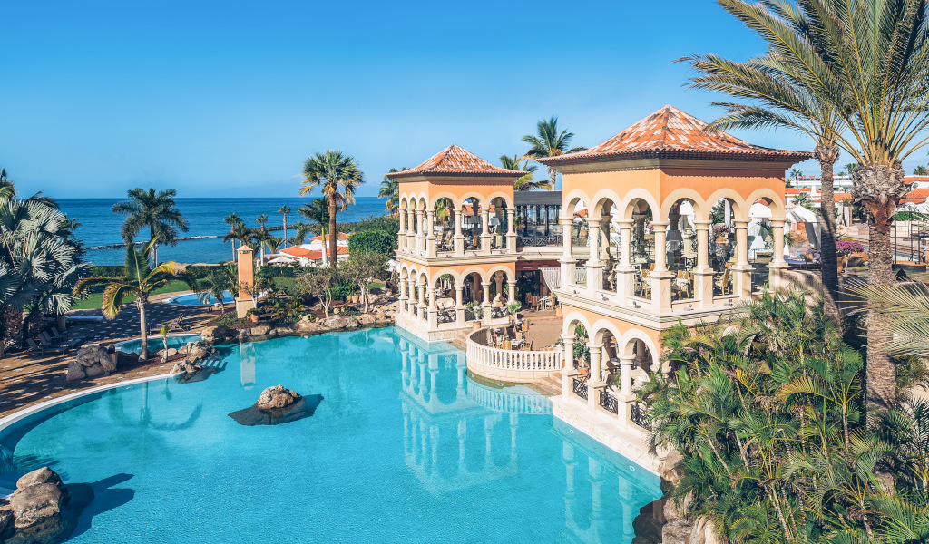 Zwembad en mediterrane gebouw in het resort van Tenerife, met palmbomen en uitzicht op zee.