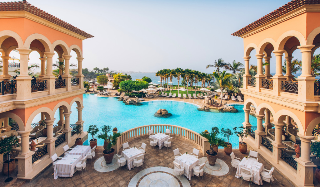 Zwembad omringd door palmbomen en arcade-gebouwen in een resort op Tenerife.