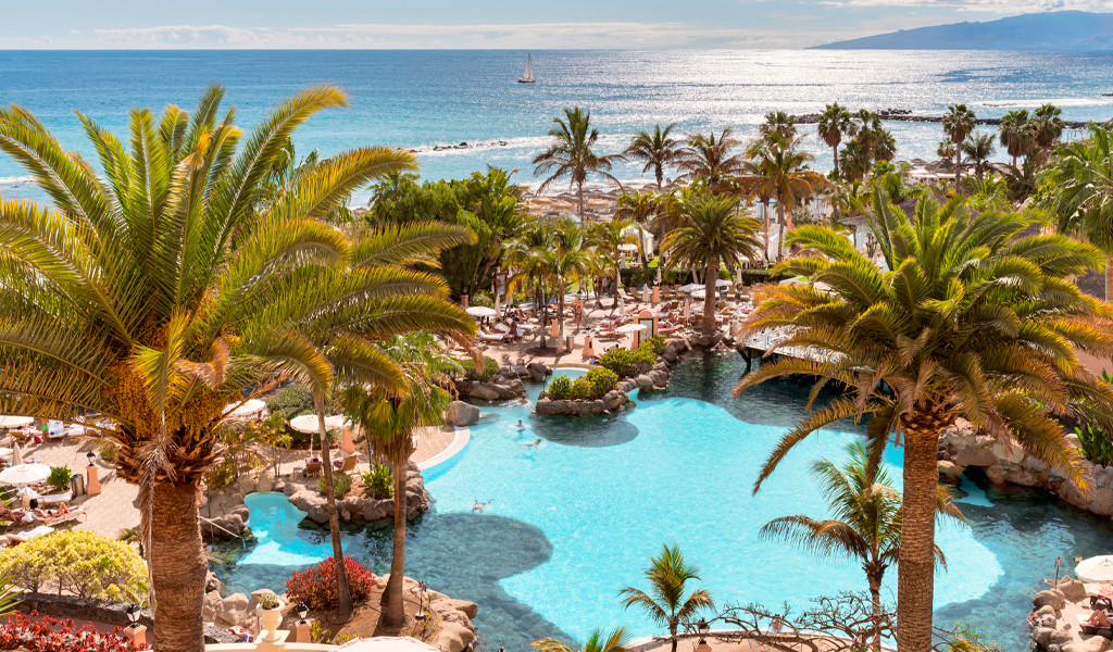 Zwembad omringd door palmbomen en zeezicht op Tenerife.