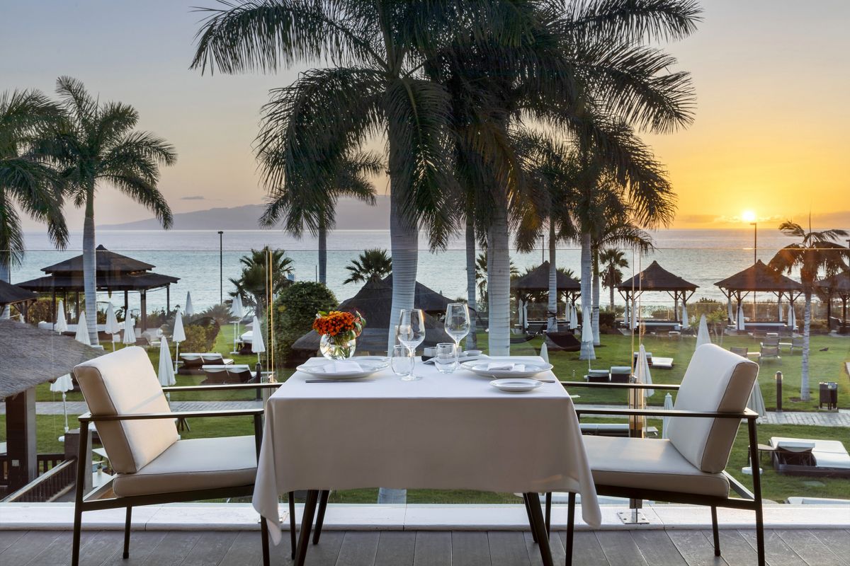 Tafel met uitzicht op de zonsondergang op het strand van Tenerife, omringd door palmbomen.