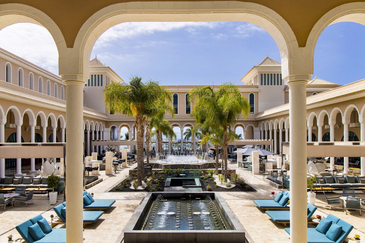 Hotelpatio op Tenerife met zwembad, palmbomen en ligstoelen.