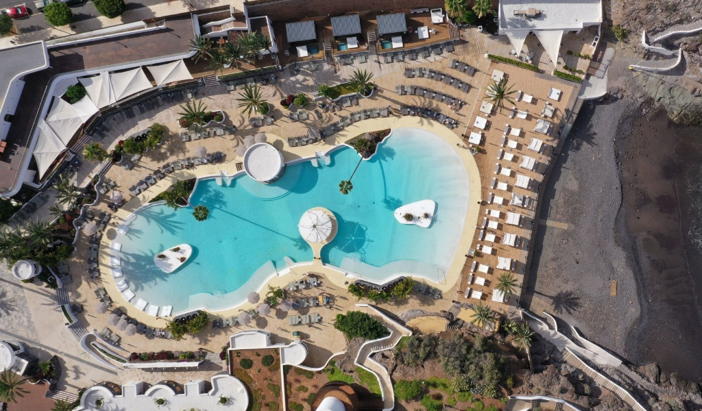 Buitenzwembad aan het strand op Tenerife, omringd door ligstoelen en palmbomen.