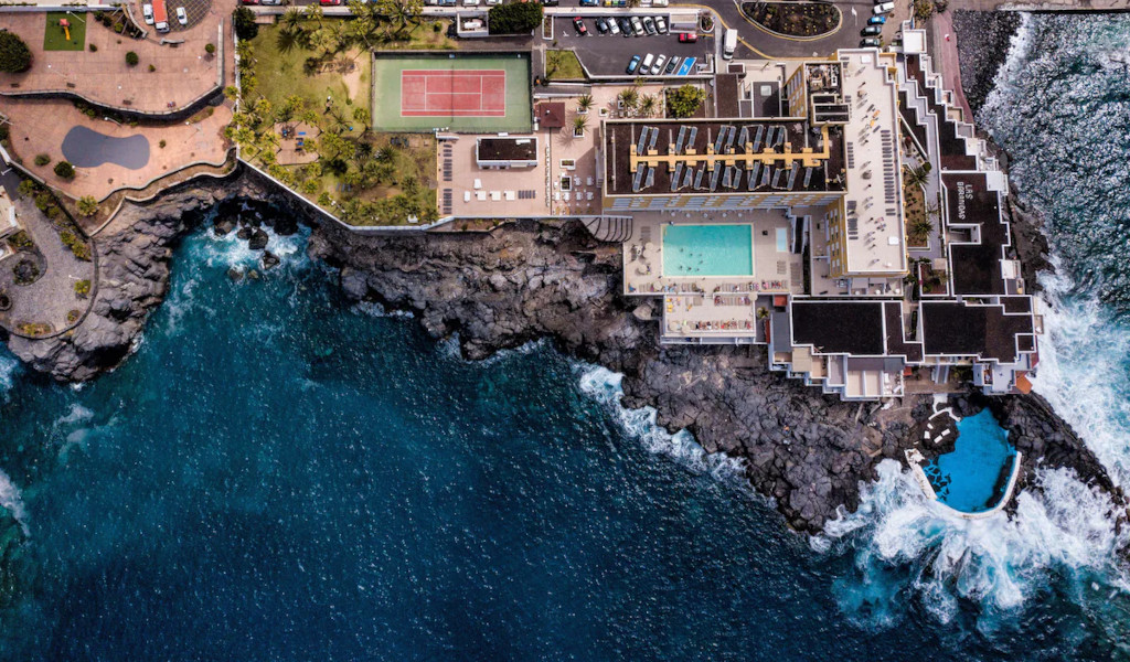 Luchtfoto van een hotel aan zee op Tenerife, met zwembad en tennisbaan.