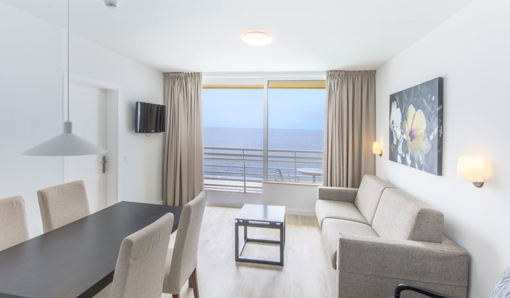 Woonkamer op Tenerife met tafel, bank, tv en uitzicht op zee.