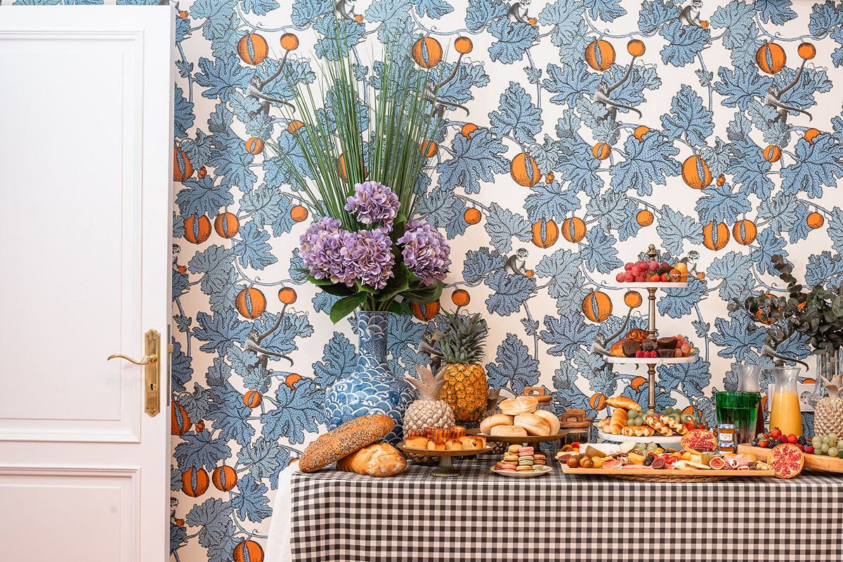 Tafel met allerlei borden met fruit, brood en zoetigheden voor het versierde behang.