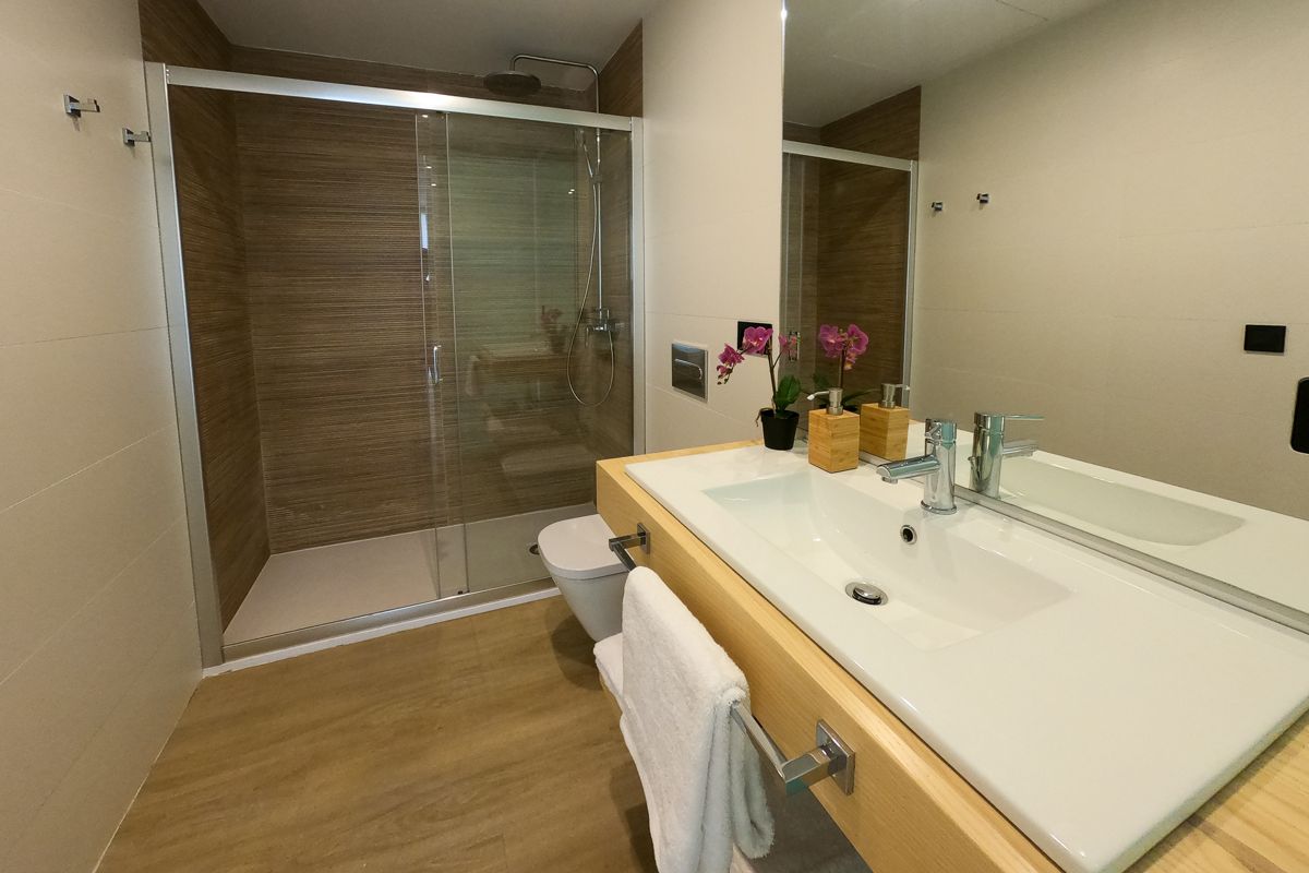 Moderne badkamer met douche, wastafel en orchideeën in een appartement op Tenerife.