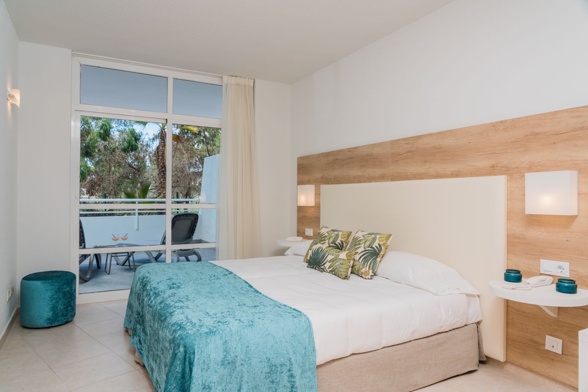 Slaapkamer met tweepersoonsbed, groene kussens, raam en terras met stoelen in Tenerife.