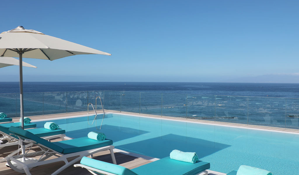 Zwembad met uitzicht op zee op Tenerife, met ligstoelen en parasols ernaast.