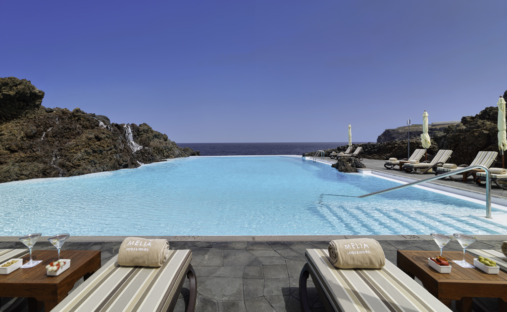 Infinity zwembad met zeezicht in een hotel op Tenerife, met ligstoelen en Meliá-handdoeken.