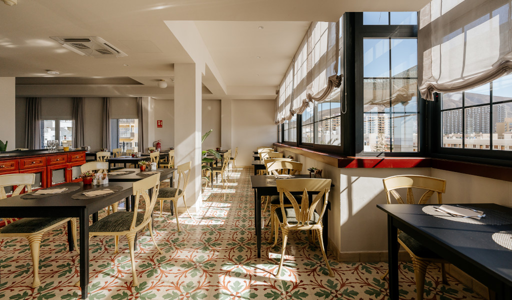 Licht restaurant met tafels en stoelen in Adeje, Tenerife, met uitzicht naar buiten.