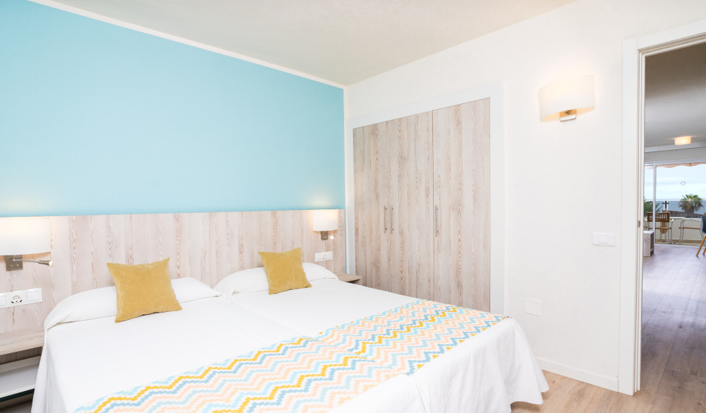 Kamer met twee bedden, blauwe muur en toegang tot een terras op Tenerife.