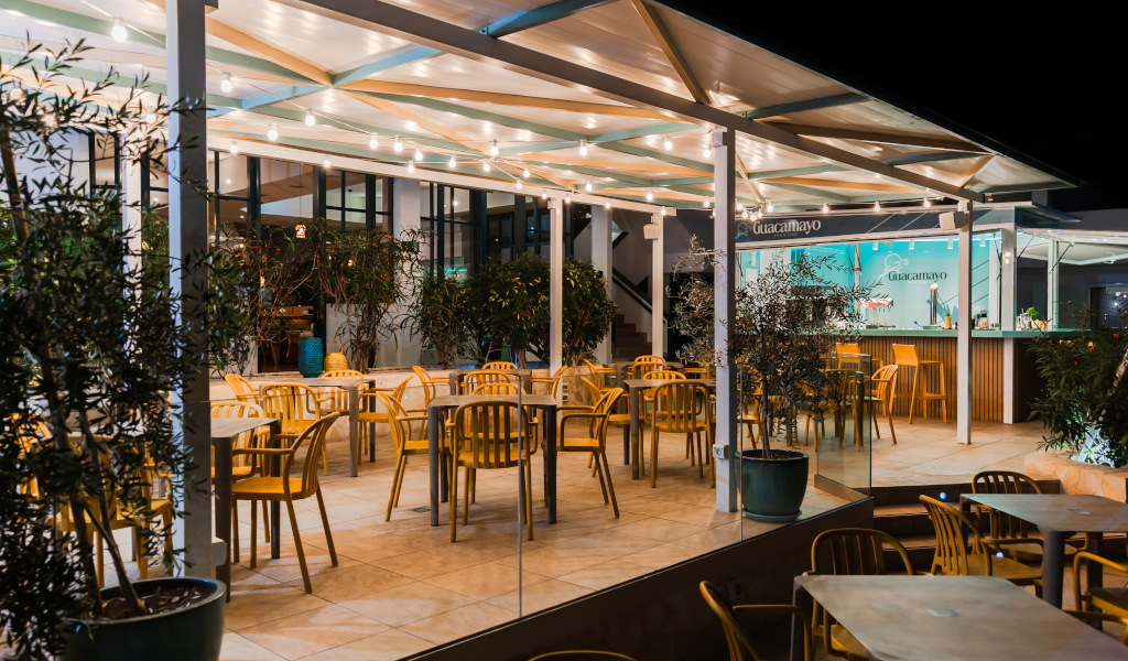 Verlicht terras van het Guacamayo-restaurant op Tenerife met lege tafels en stoelen.