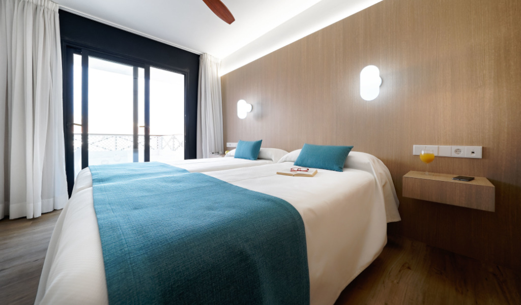 Hotelkamer op Tenerife met tweepersoonsbed, witte lakens en blauwe kussens.