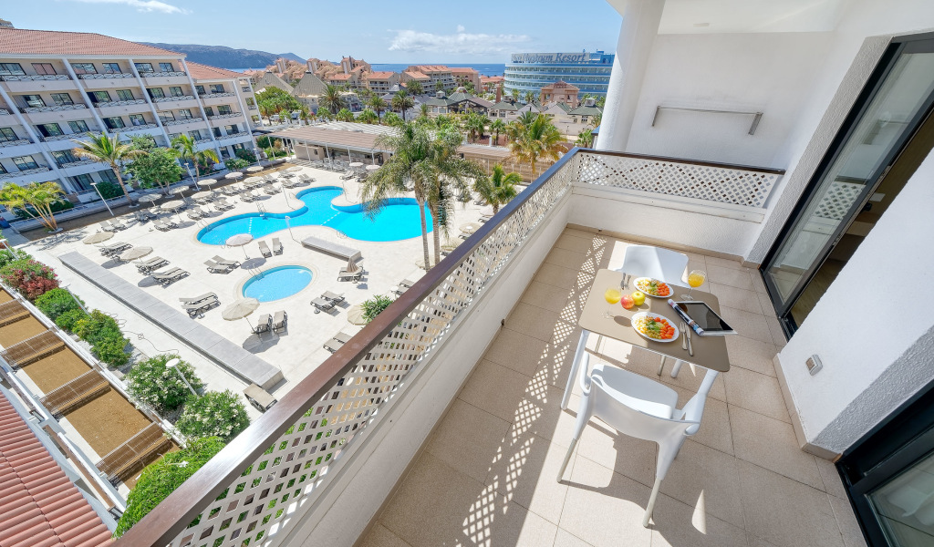 Balkon met uitzicht op het hotelzwembad op Tenerife, tafel met gerechten en drankjes.