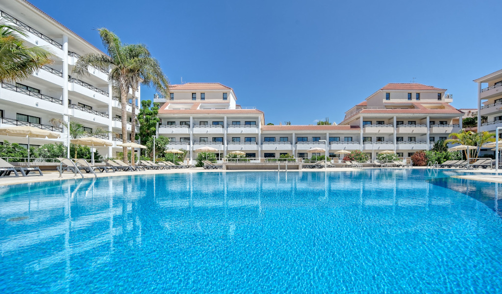 Zwembad voor het hotelgebouw op Tenerife met palmbomen en ligstoelen.