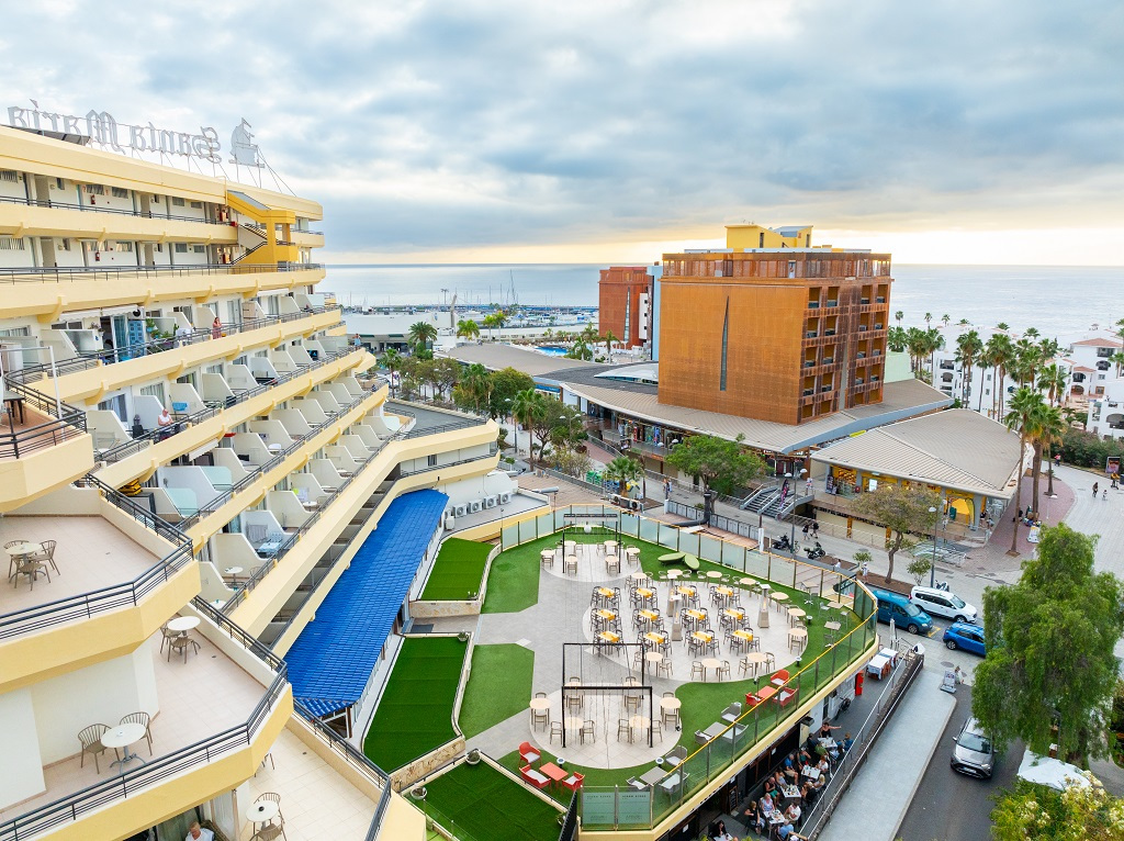 Panoramisch uitzicht op een hotel op Tenerife met de oceaan op de achtergrond en een terras met tafels.