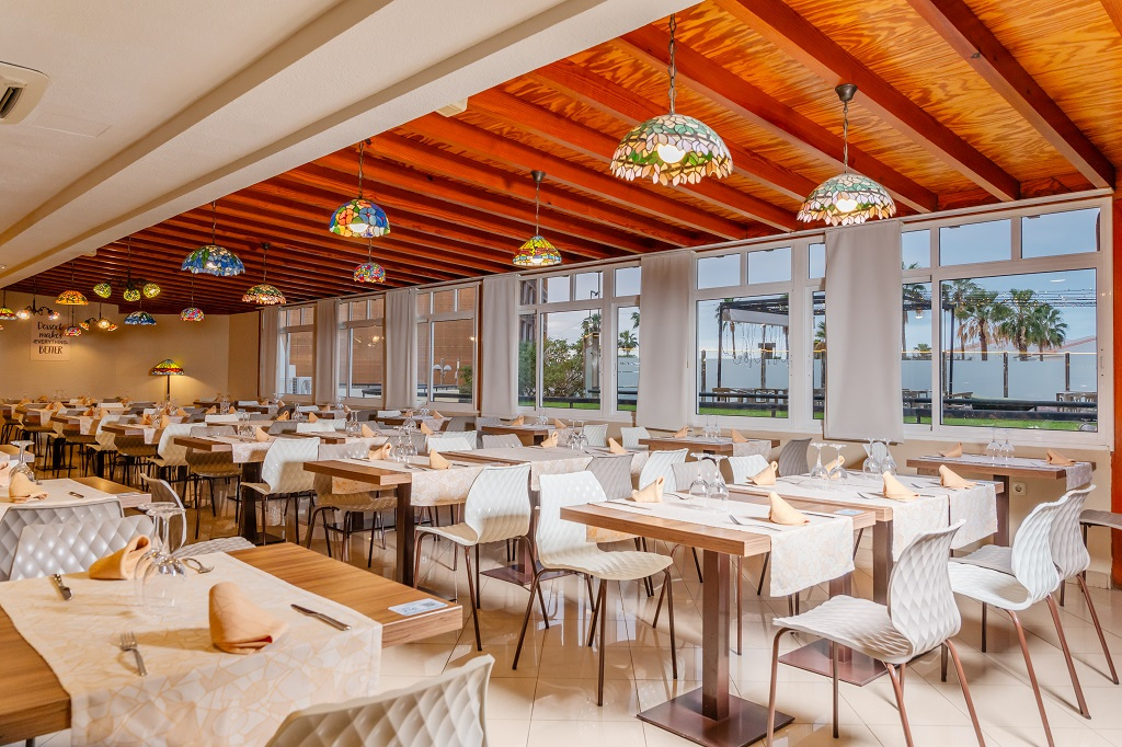 Ruim restaurant op Tenerife, voorbereide tafels en uitzicht naar buiten met palmbomen.