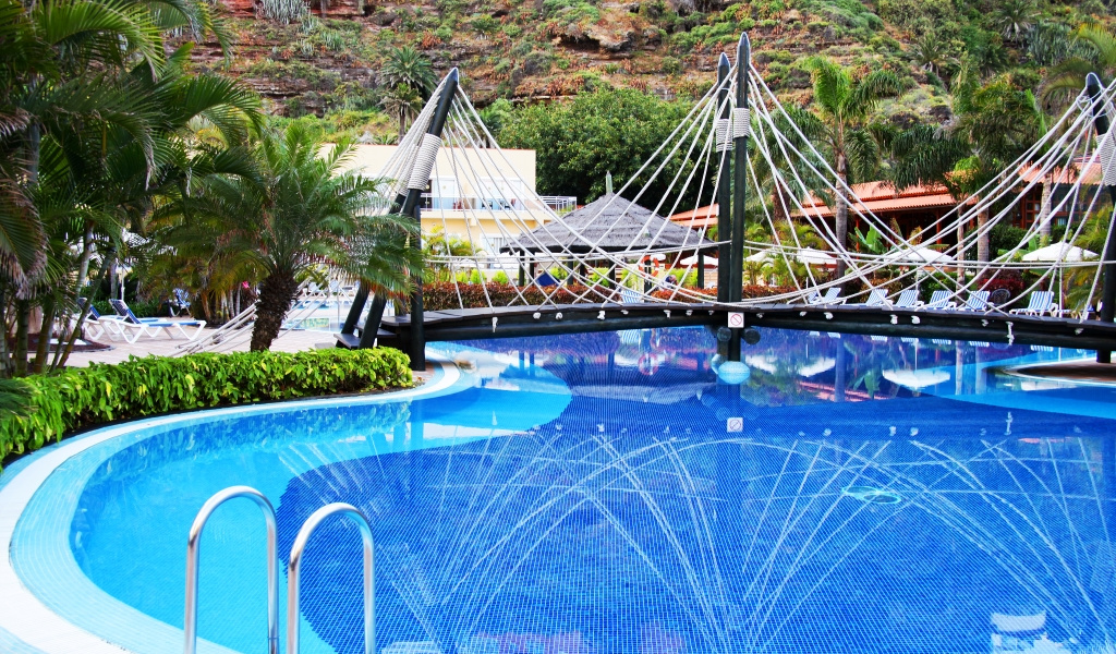 Zwembad met hangbrug in een hotel op Tenerife, omringd door palmbomen.