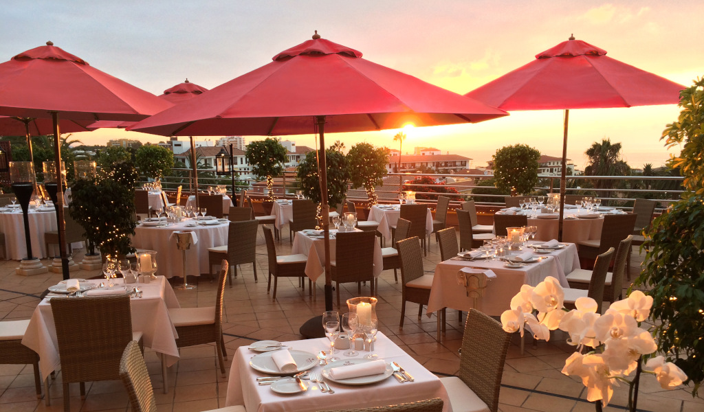 Restaurantterras op Tenerife bij zonsondergang met rode tafels en parasols.