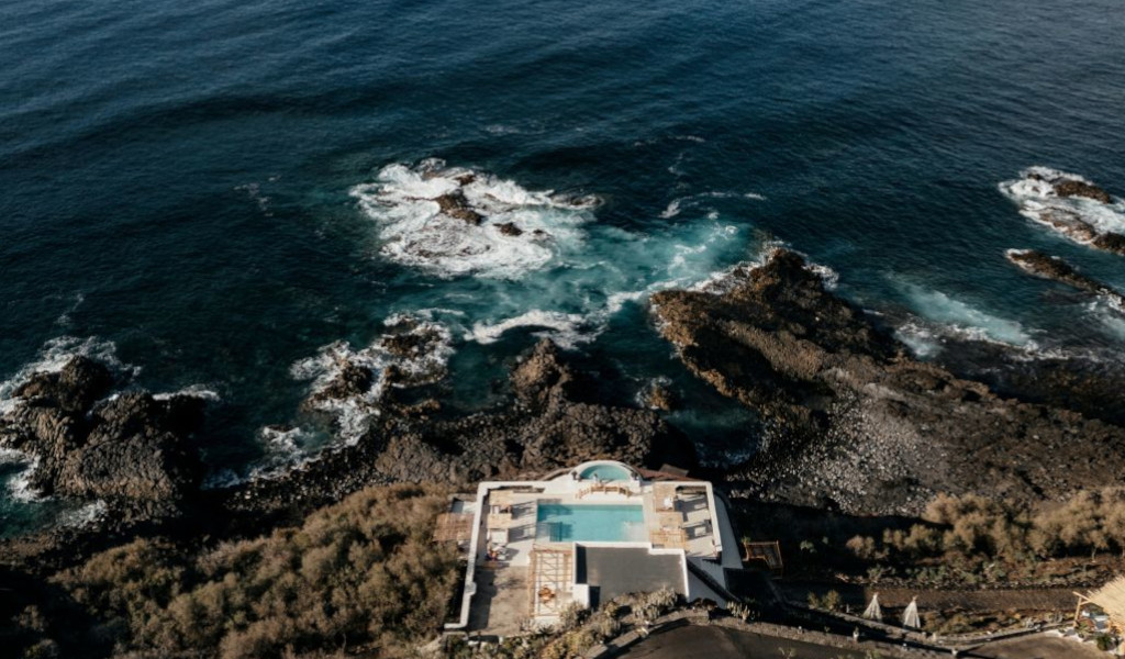 Zwembad en oceaan aan de kust van Tenerife, omringd door rotsen en vegetatie.