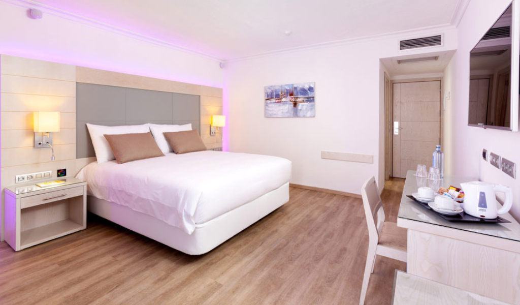 Moderne hotelkamer op Tenerife met een tweepersoonsbed, bureau en een foto aan de muur.