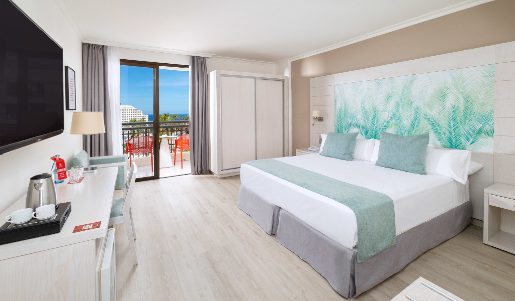 Hotelkamer op Tenerife met tweepersoonsbed, bureau en balkon met uitzicht op zee.