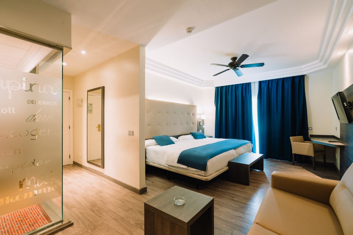 Hotelkamer op Tenerife met tweepersoonsbed, bank en blauwe gordijnen.