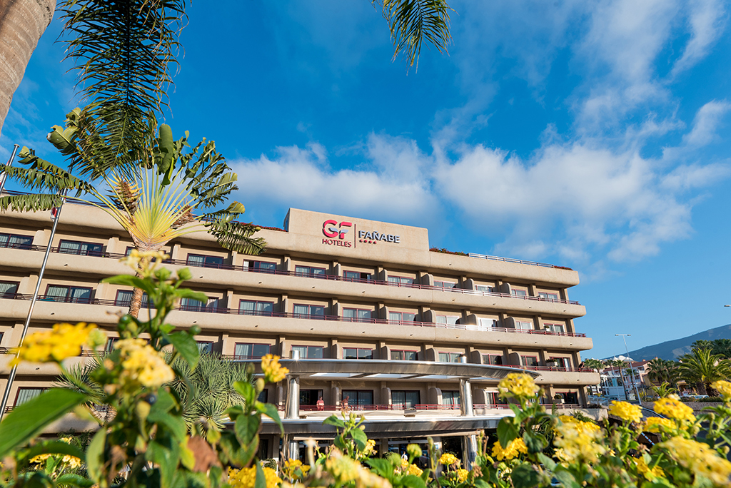 Hotel GF Fañabé op Tenerife met bloemen en palmbomen op de voorgrond.