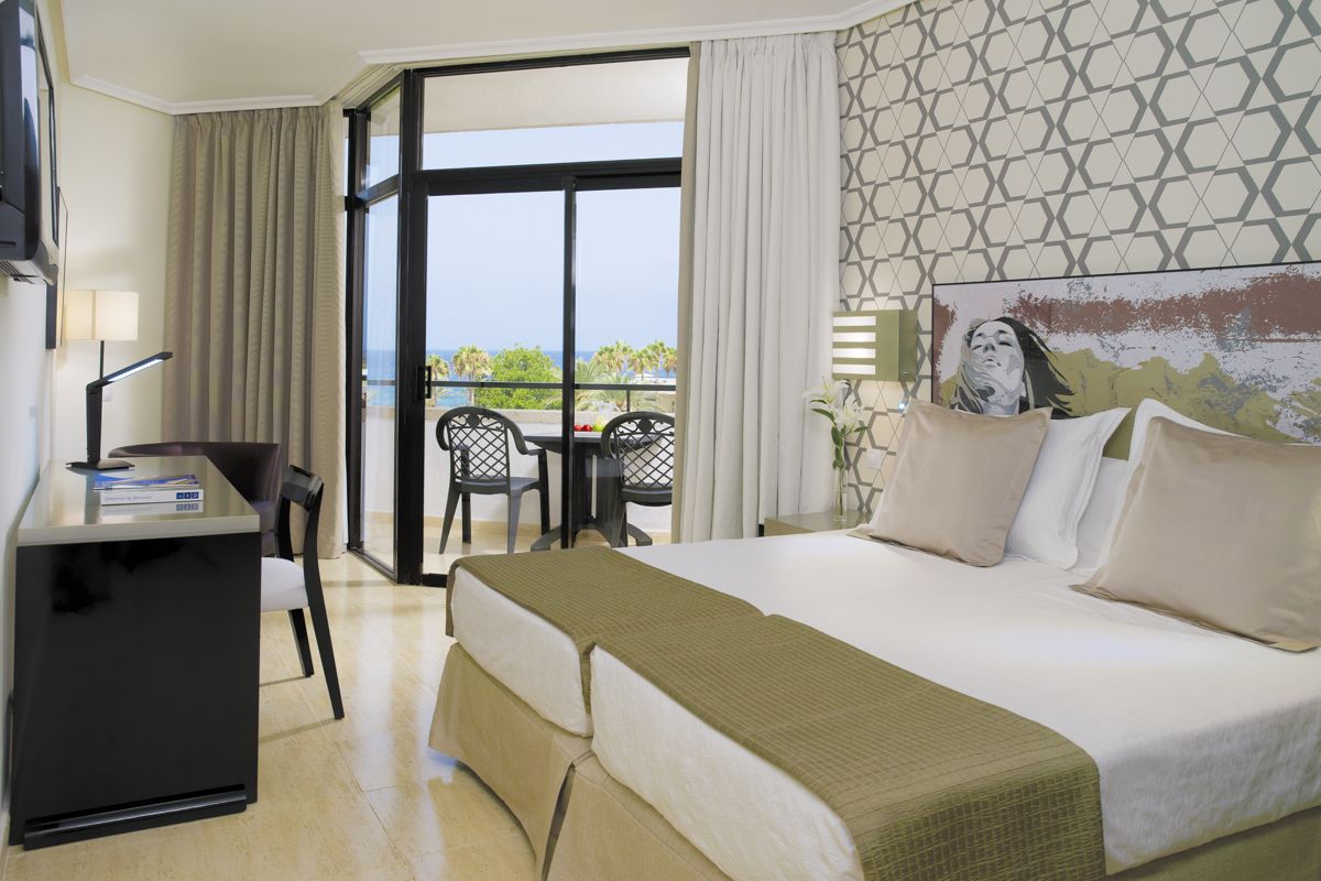 Hotelkamer op Tenerife met bed, bureau en balkon met uitzicht op zee.